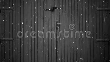 黑色和白色的噪音视频，大雪花在冬天落在一个旧的木制车库门前，大金属铰链